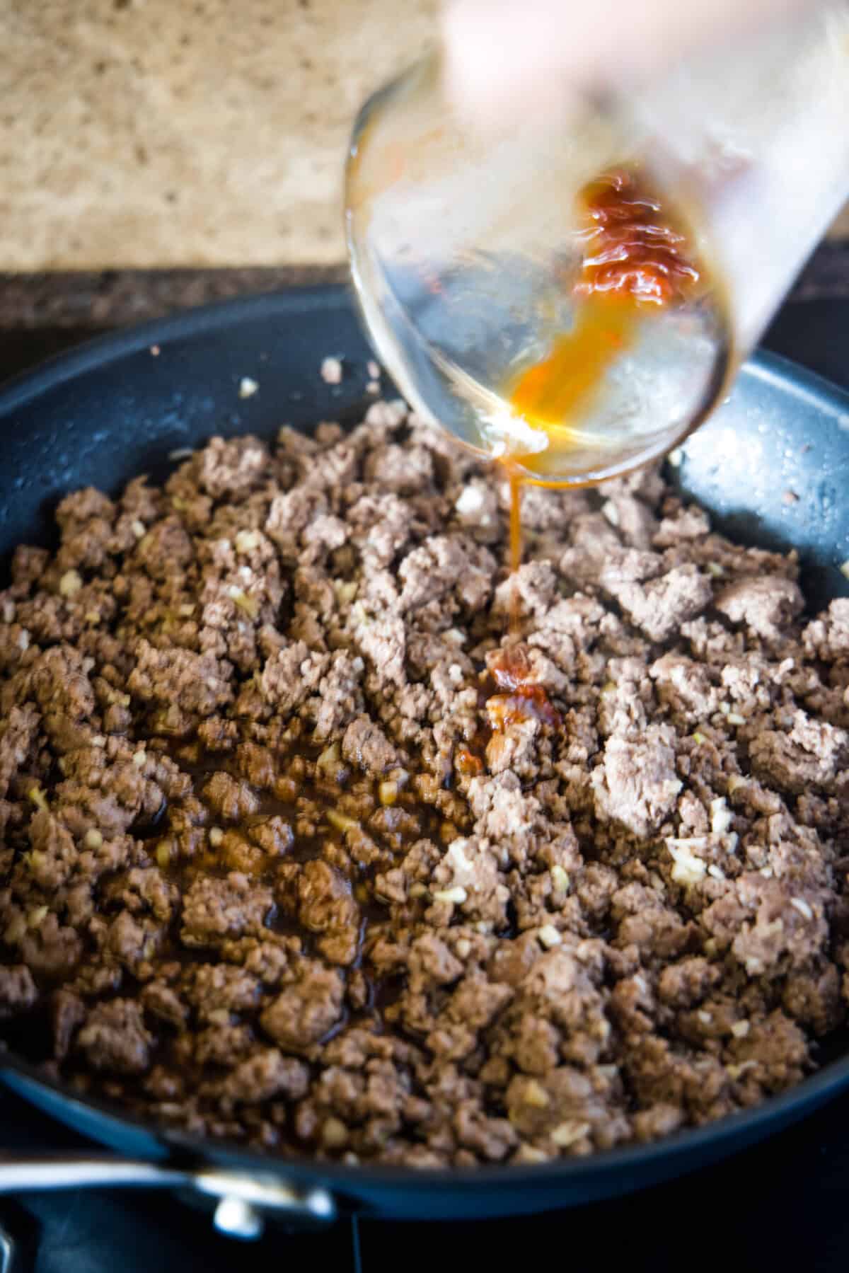 adding sauce to beef in a skillet