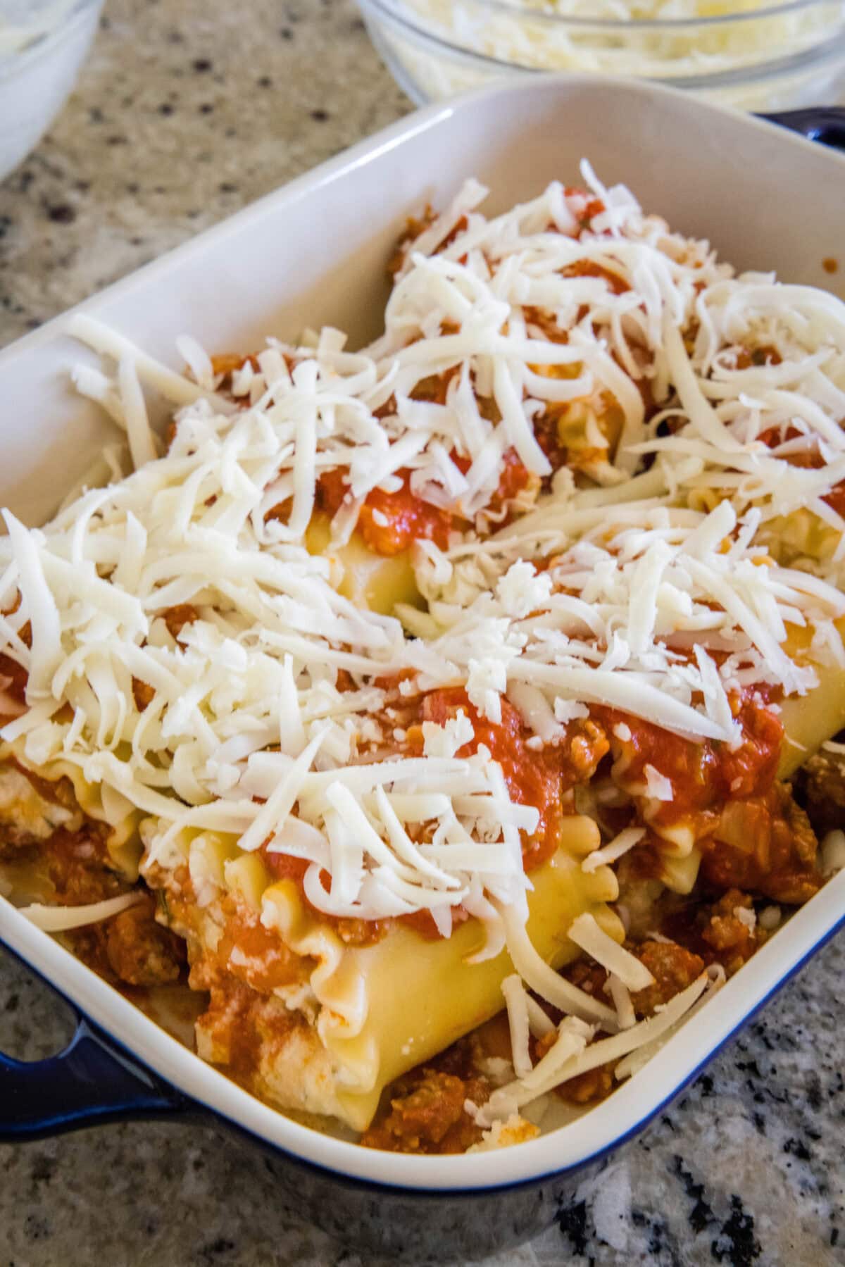 Unbaked lasagna roll ups topped with shredded cheese in a baking dish.