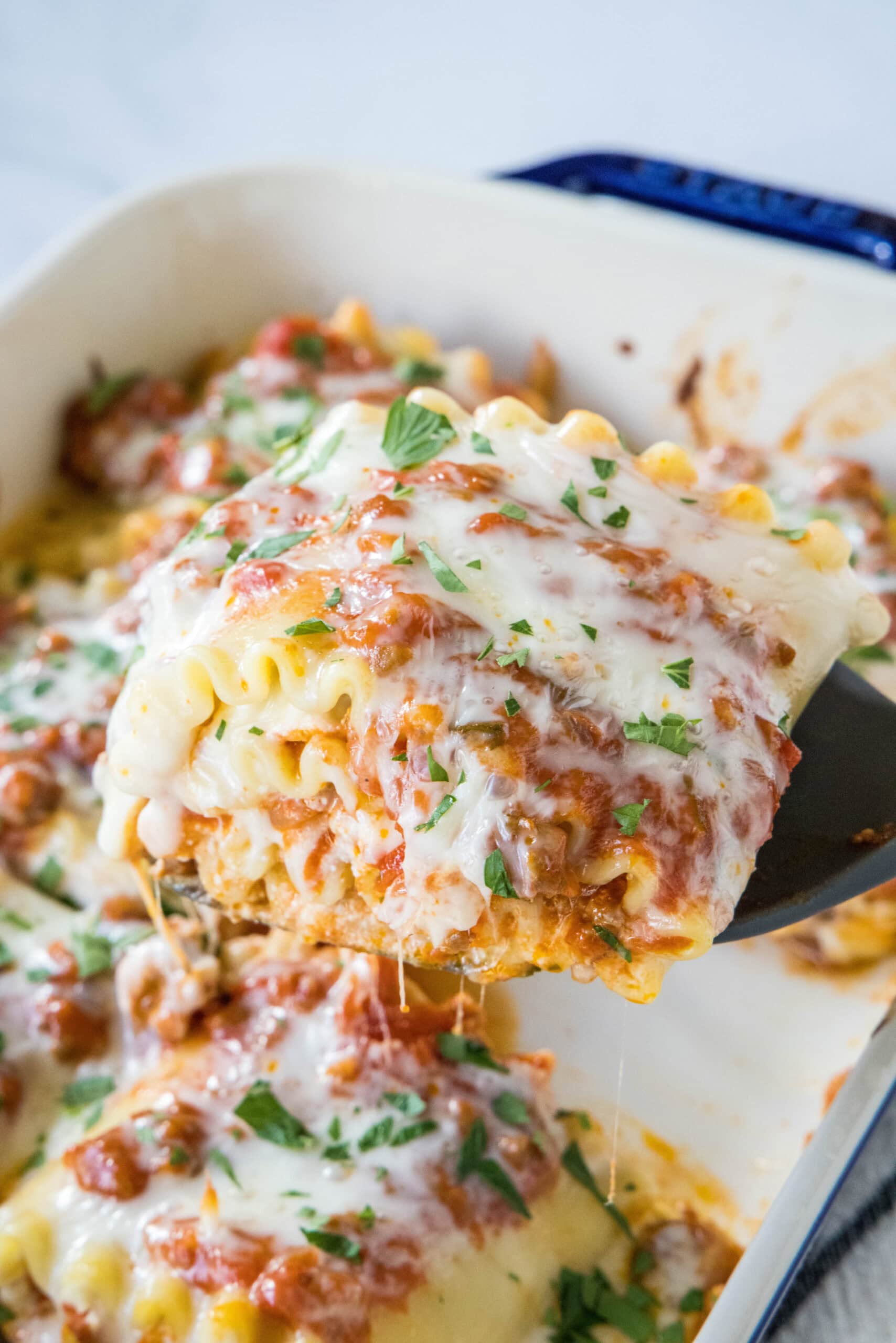 A spatula lifting a lasagna roll up from a baking dish.