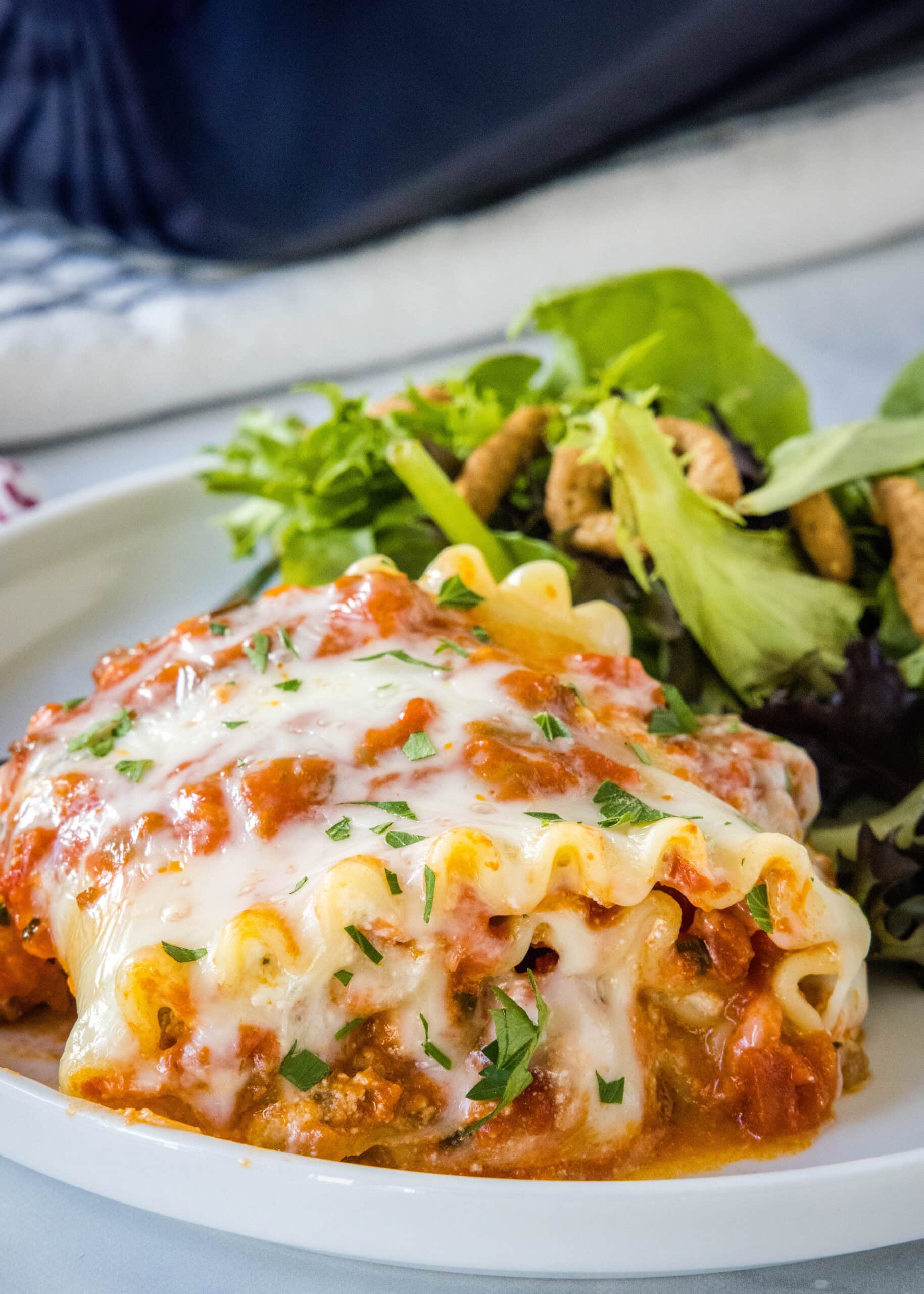 A lasagna roll up served on a plate with green salad on the side.