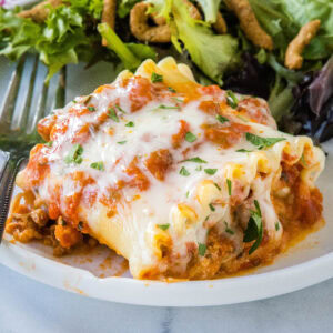 A lasagna roll up served on a plate with green salad on the side.