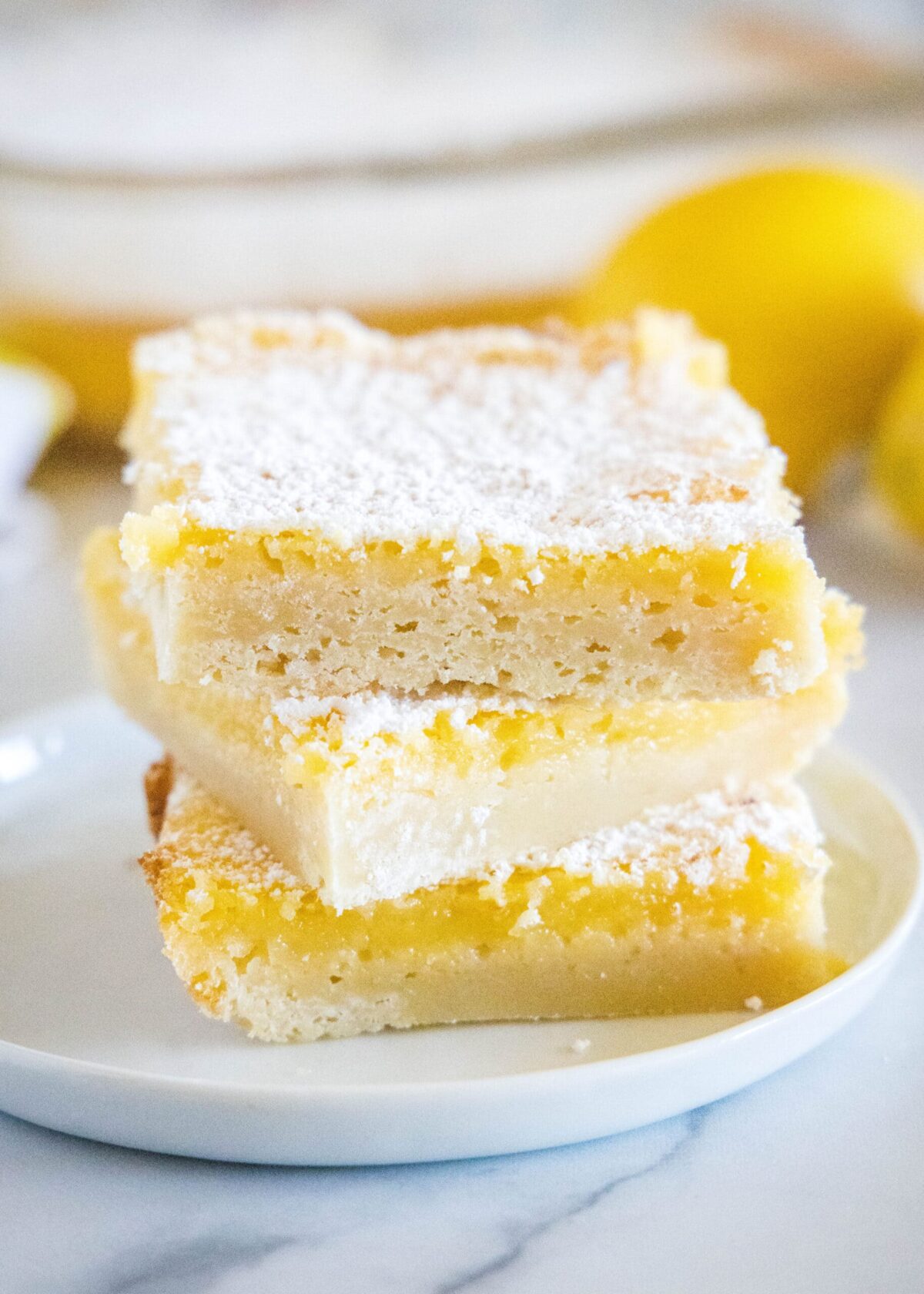 These easy lemon bars have a tart filling, a buttery crust, and are perfect for parties. And they only take 1 hour to make! Close up of three lemon bars stacked on a plate