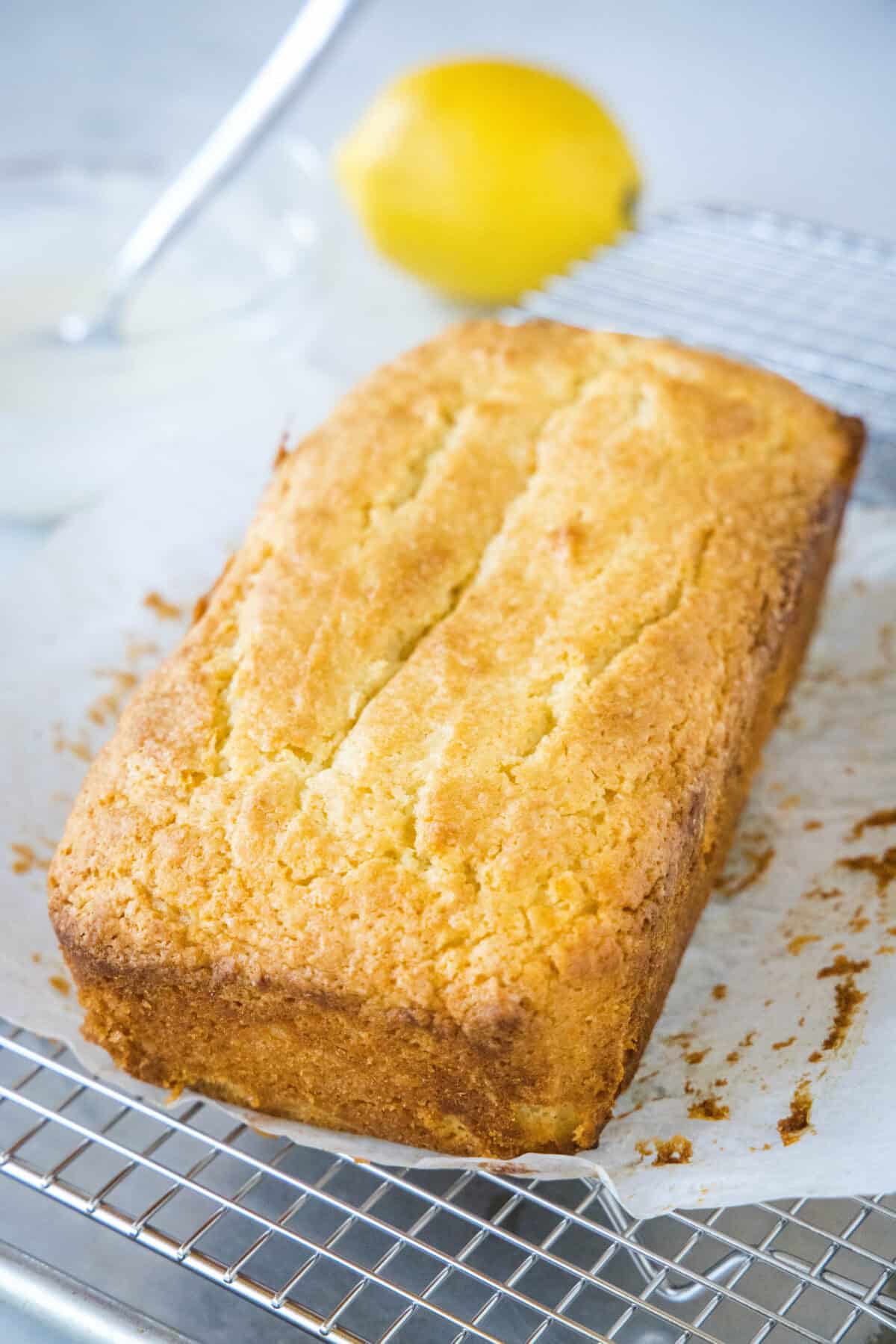 Baked lemon loaf on a sheet of parchment paper on top of a wire rack.