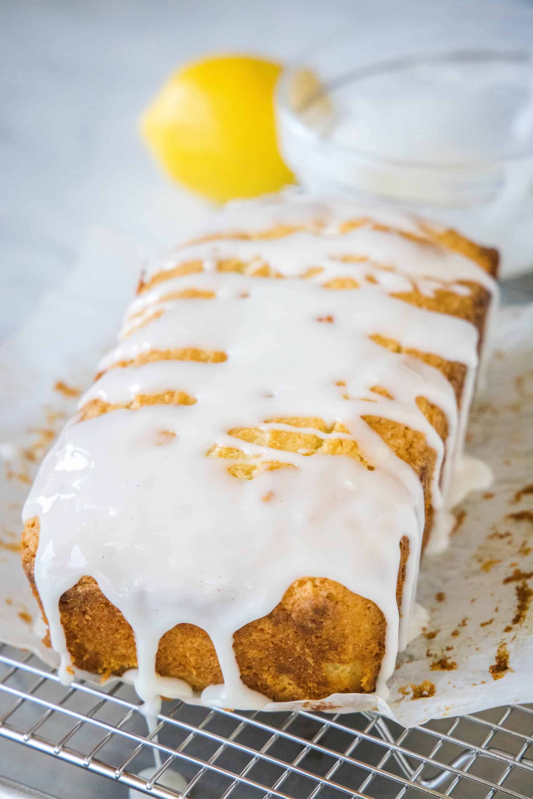 Glazed lemon loaf on a sheet of parchment paper on top of a wire rack.