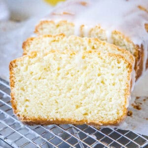 Glazed lemon loaf with two slices cut from the end on a wire rack.