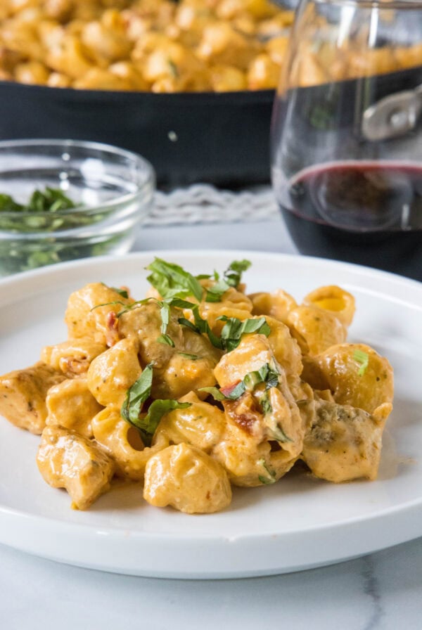 A serving of Marry Me Chicken pasta on a white plate, with the rest of the pasta in a skillet in the background.