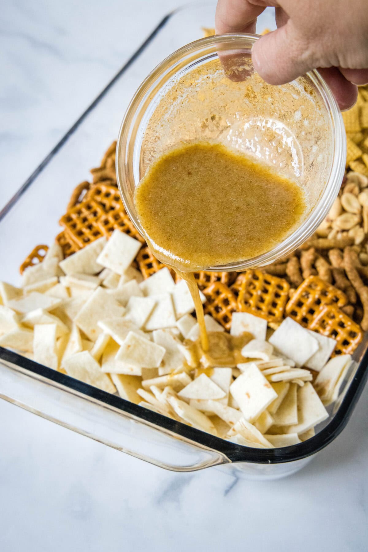 pouring butter mixture over snack mix in baking dish