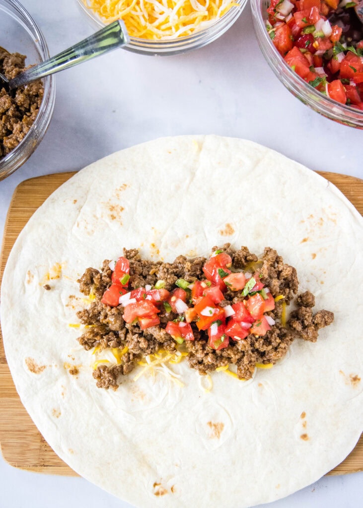 putting pico de gallo over ground beef in a tortilla