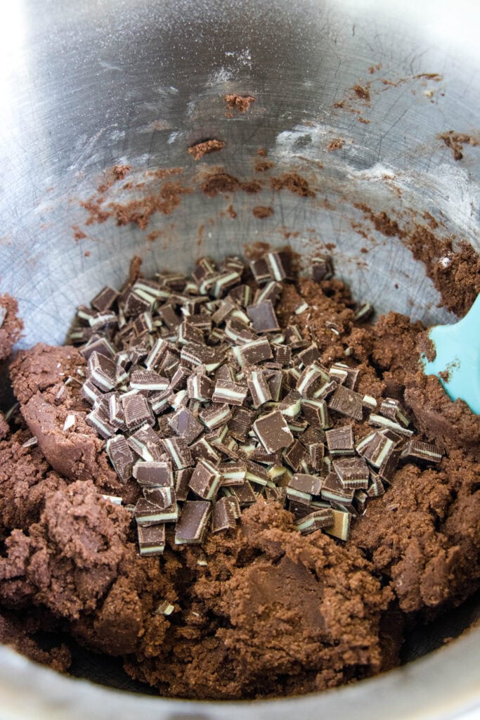 adding andes mint to chocolate cookie dough in a mixing bowl