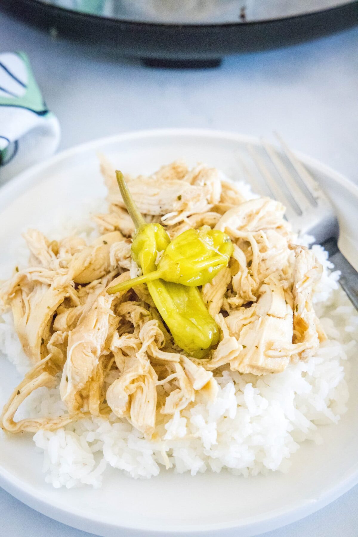This slow cooker Mississippi chicken recipe is juicy, tender, and full of rich ranch and onion soup mix, with a kick of spice. A plate with a fork and a bed of rice, topped with shredded chicken and pepperoncini peppers