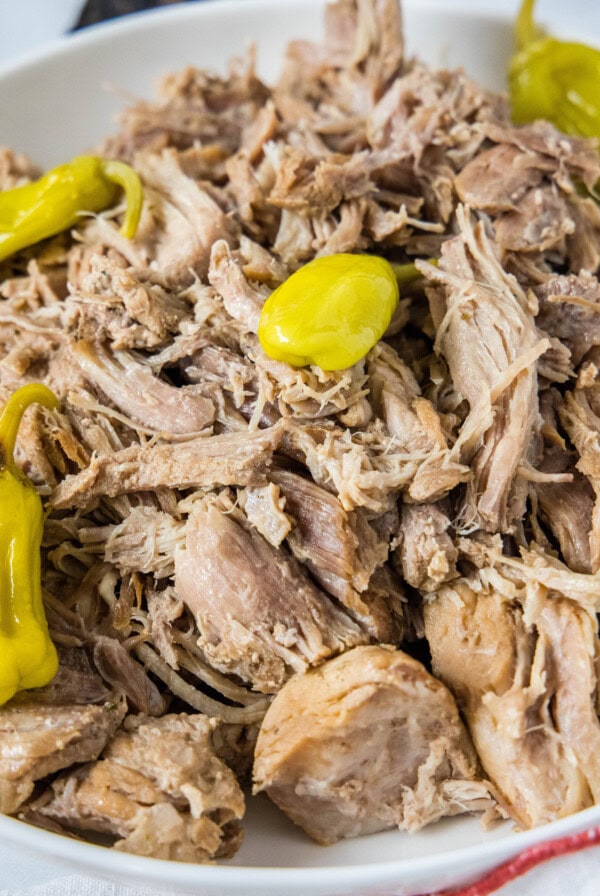 A bowl of shredded pork topped with pepperoncini peppers