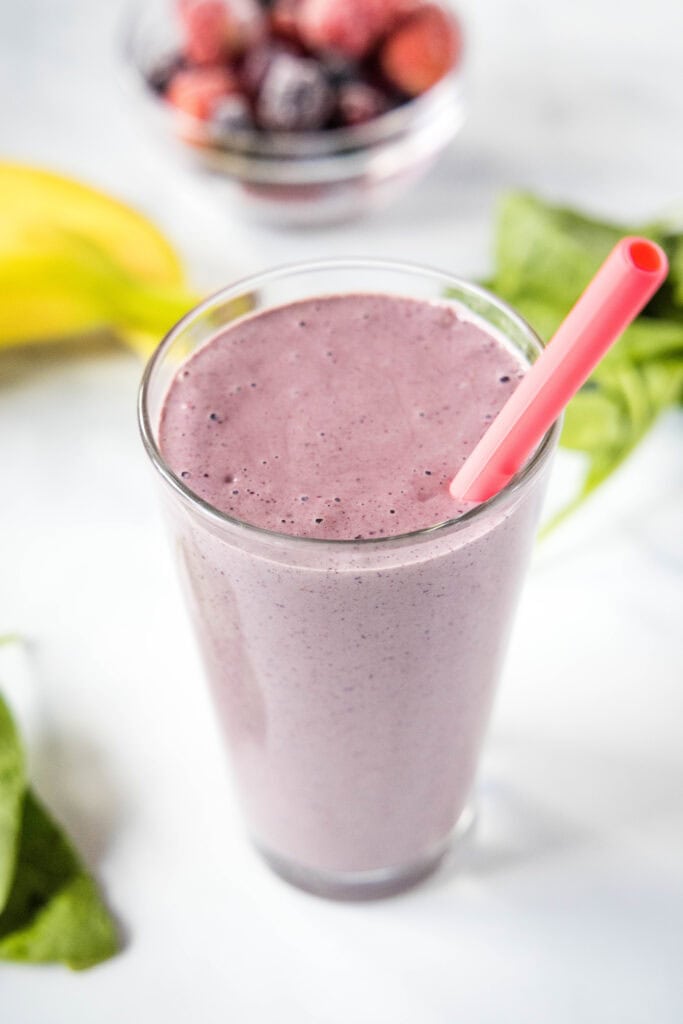 mixed berry smoothie in a glass with pink straw