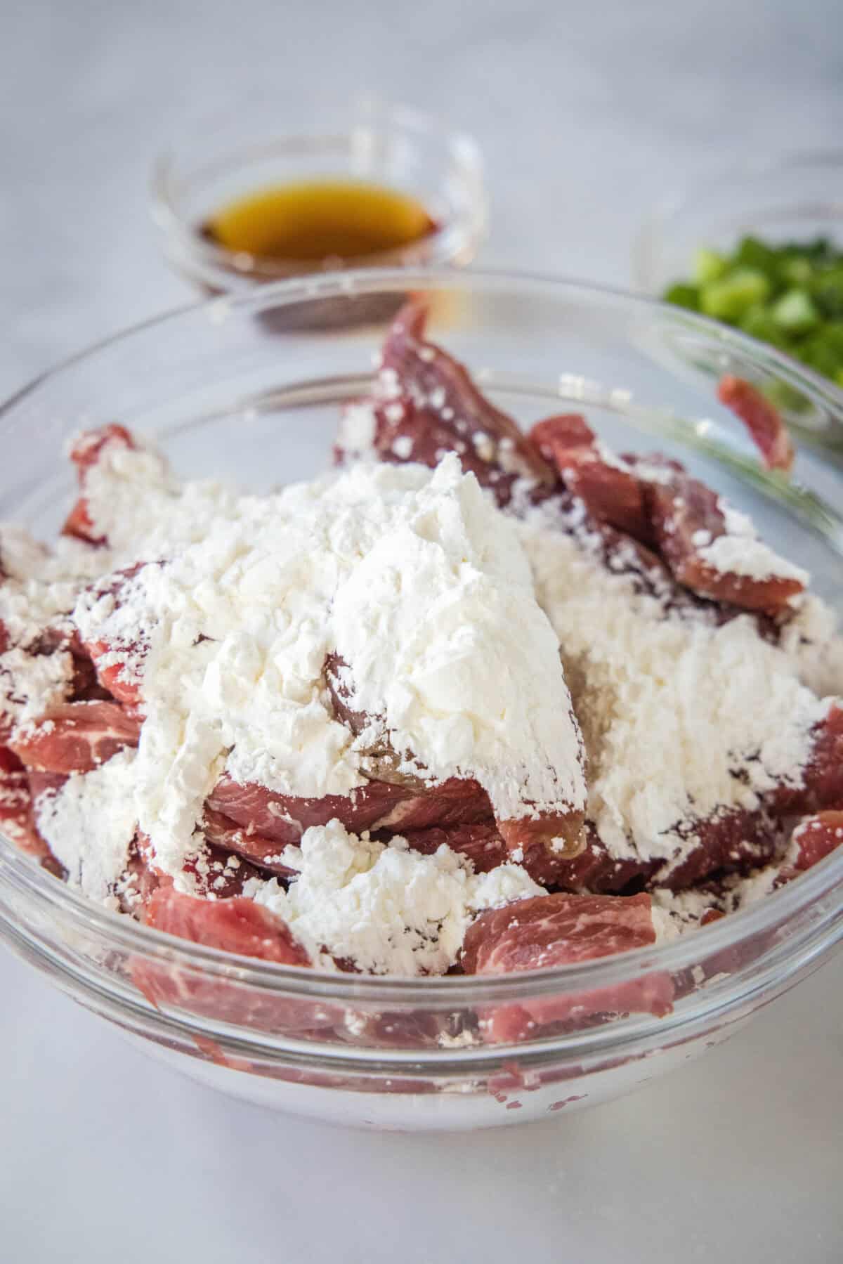 Beef strips combined with cornstarch in a bowl.