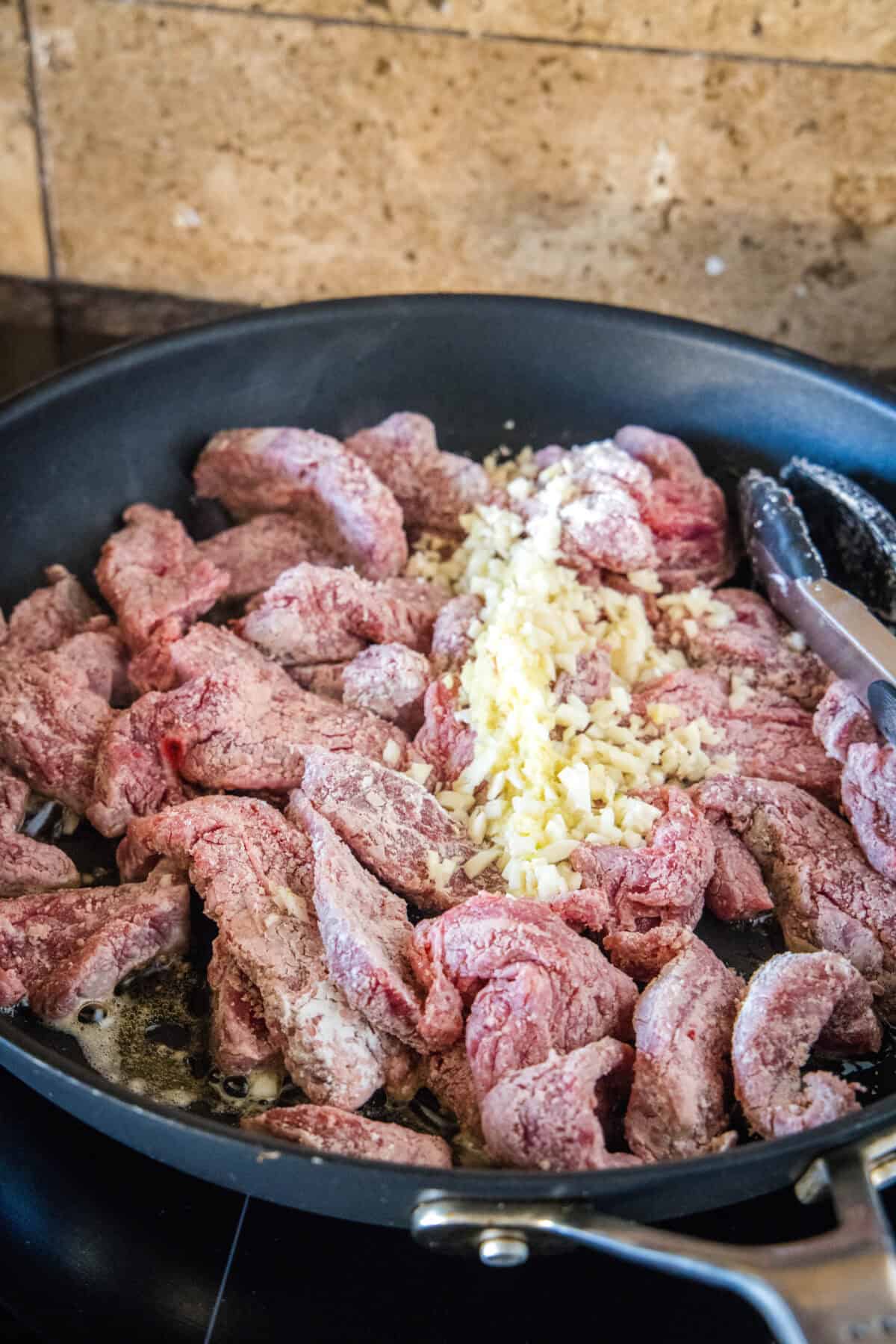 Beef strips added to a skillet with garlic and ginger.