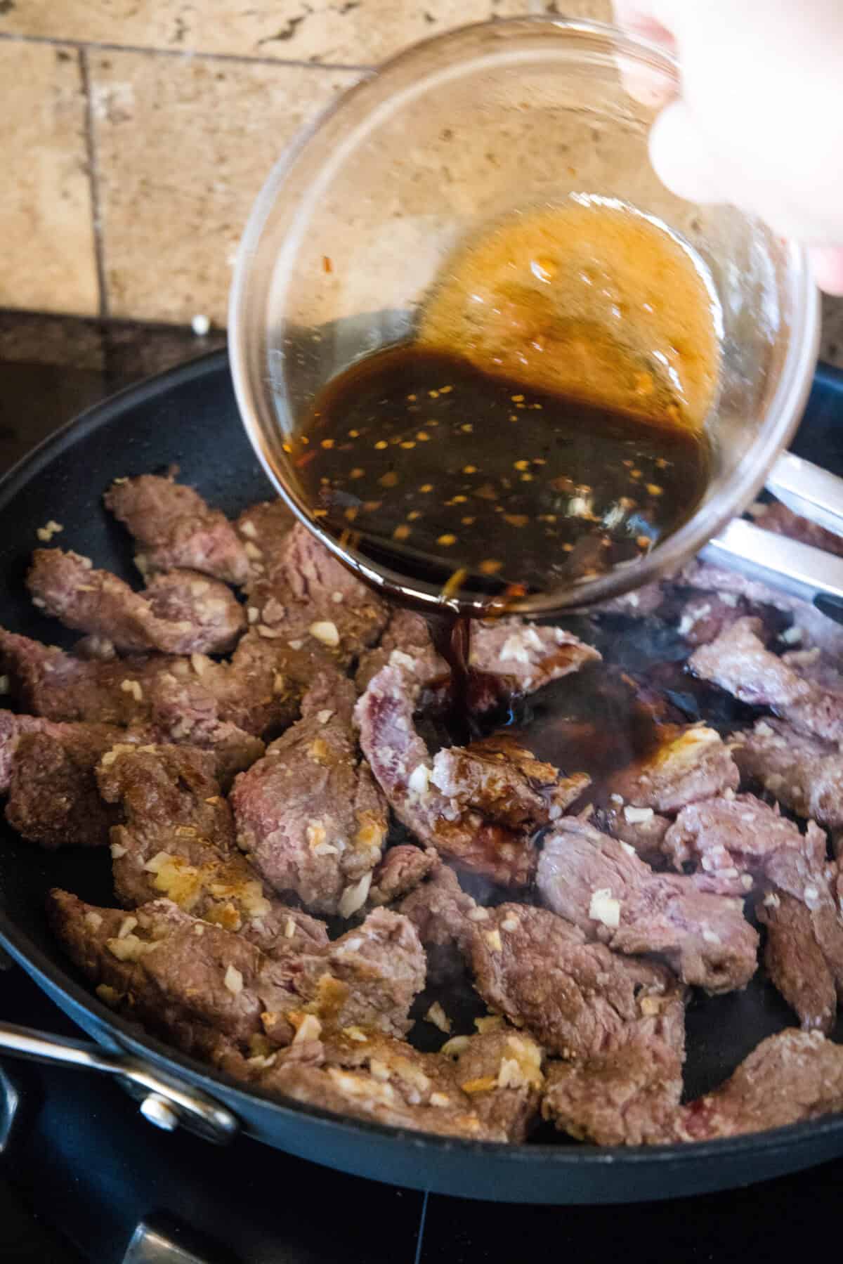 Pouring stir-fry sauce over crispy beef strips in a large skillet.