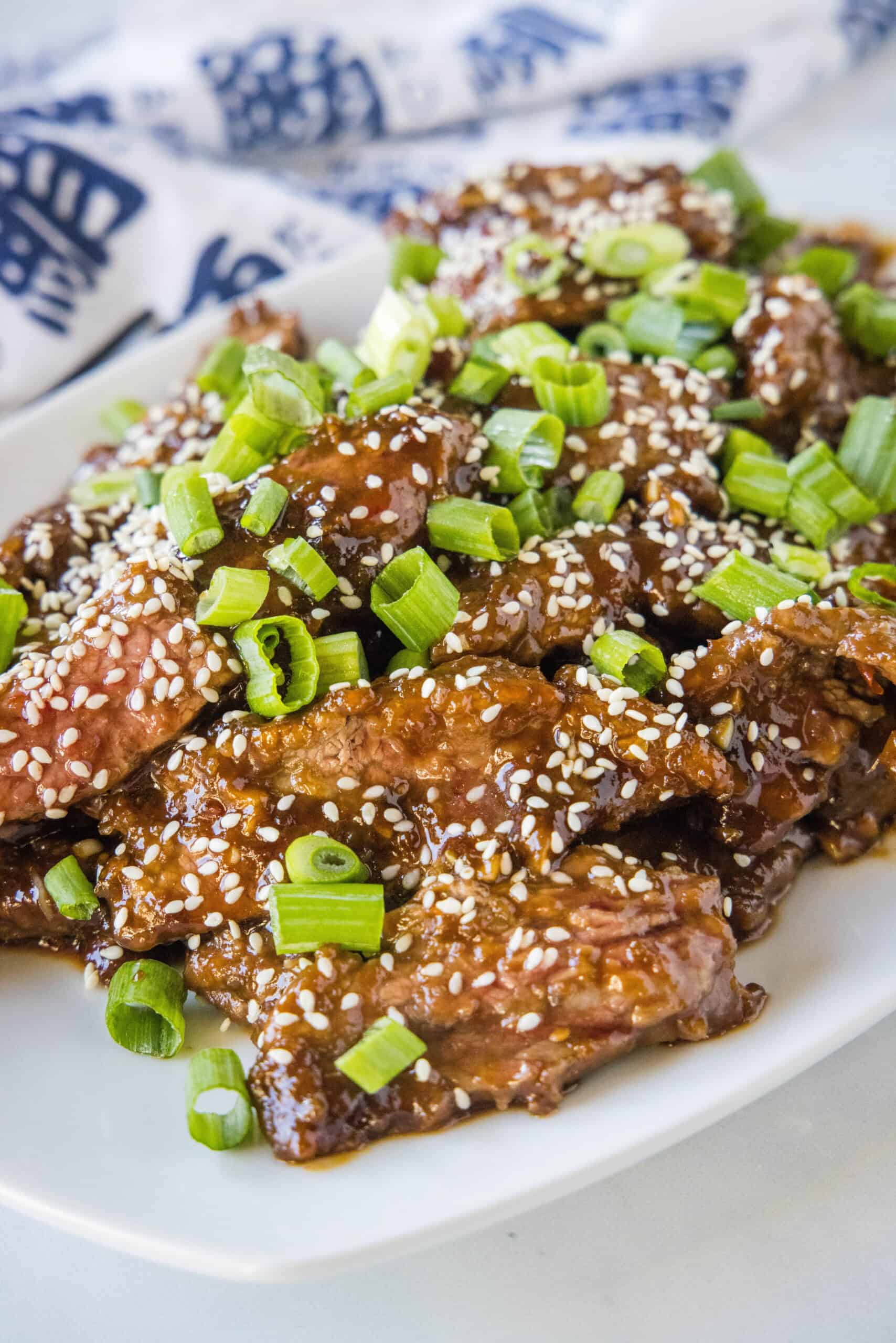 Mongolian beef topped with sesame seeds and green onions on a white platter.