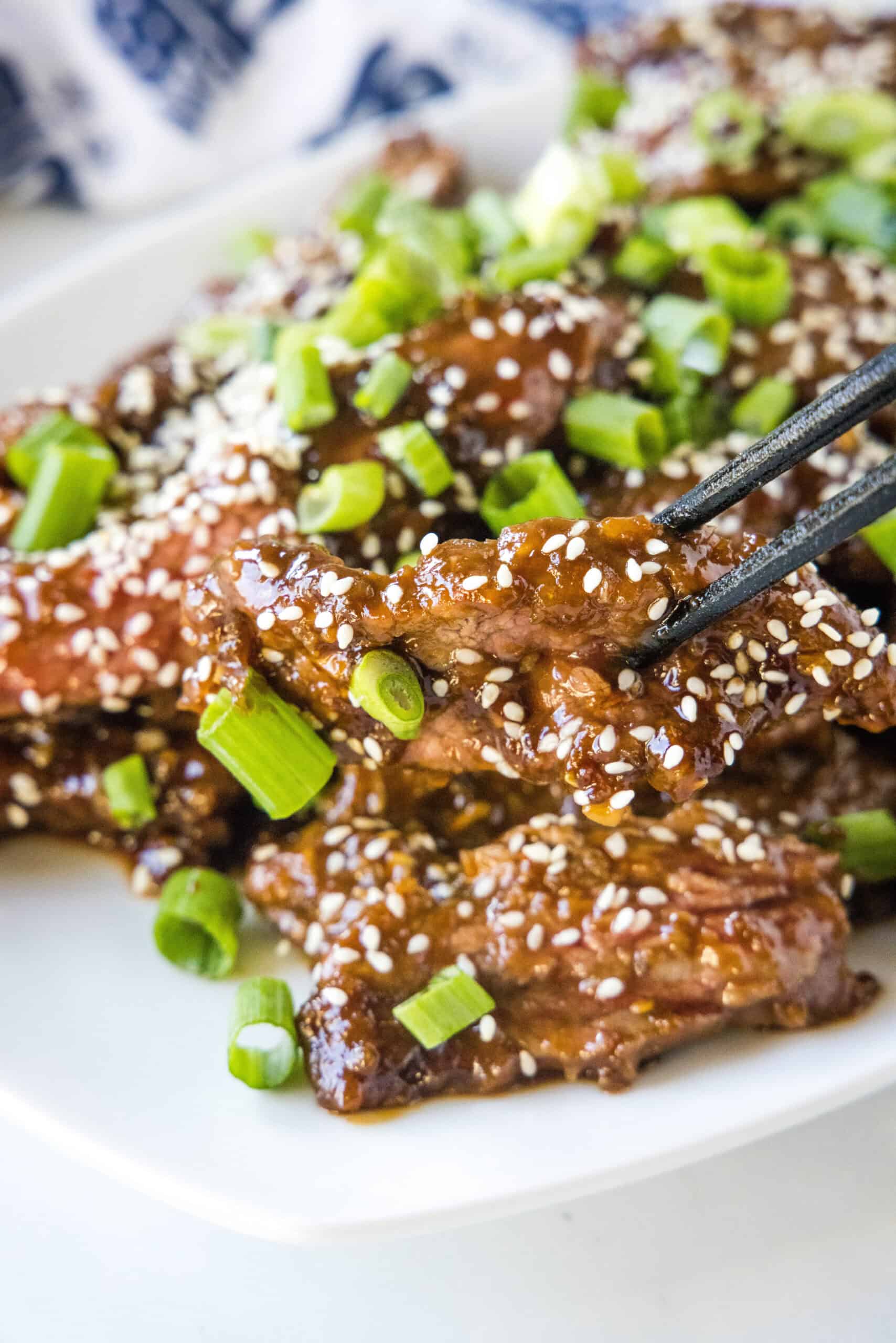 Mongolian beef topped with sesame seeds and green onions on a white platter.