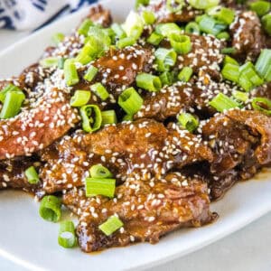 Mongolian beef topped with sesame seeds and green onions on a white platter.