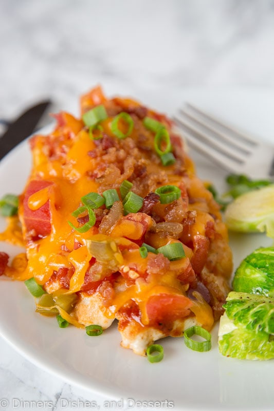 A close up of a plate of food with chicken topped with tomatoes, bacon and melted cheese