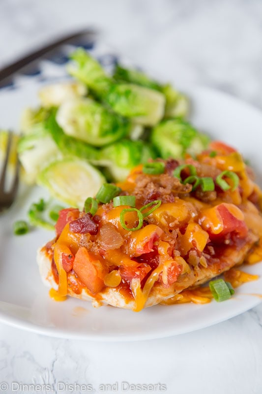 A close up of a plate of food with chicken topped with tomatoes, bacon and melted cheese