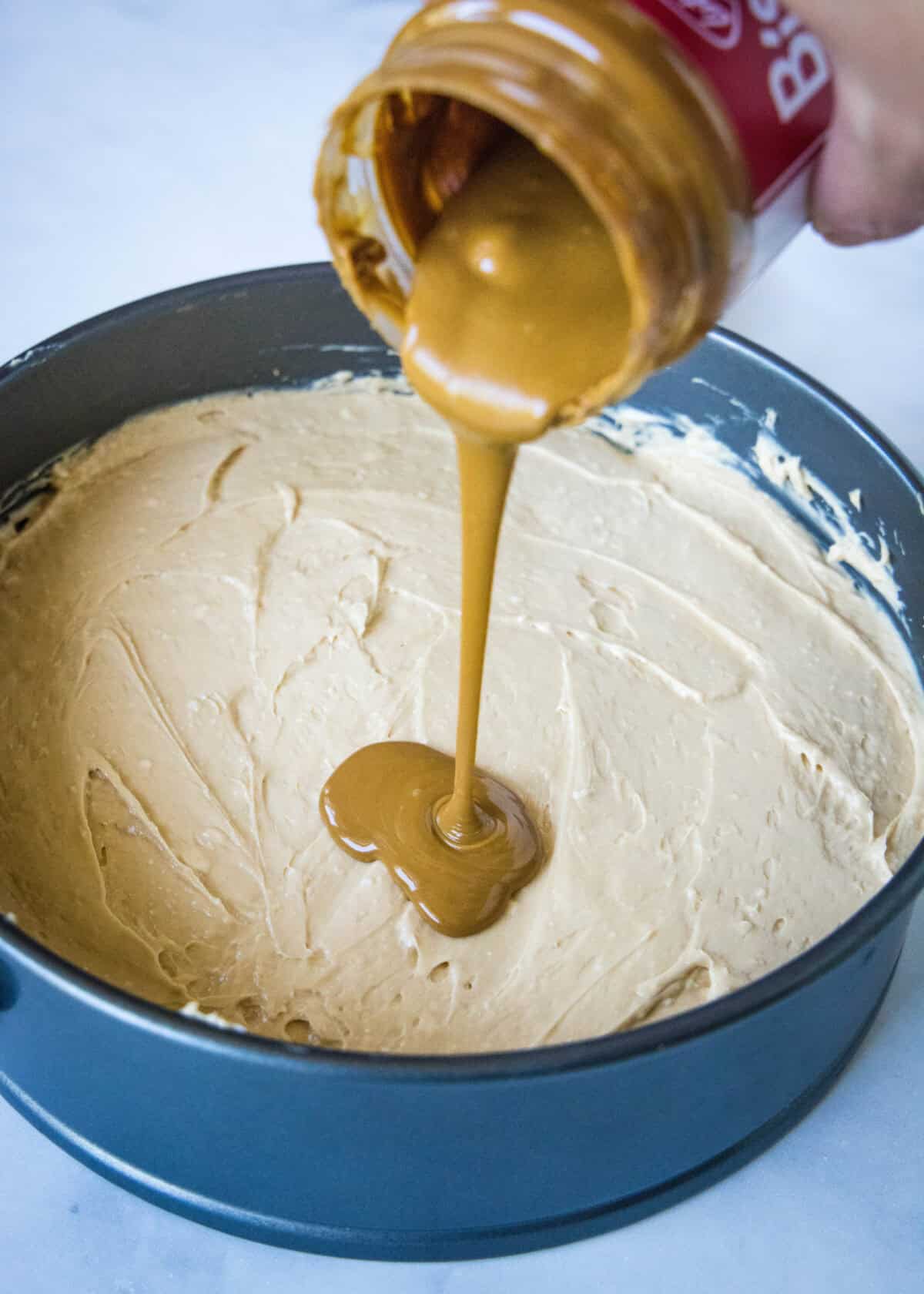 pouring biscoff spread over cheesecake layer