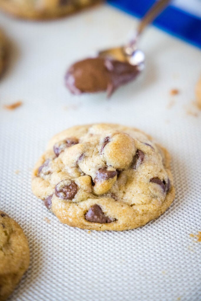 baked chocolate chip cookie on baking sheet with spoonful of nutella