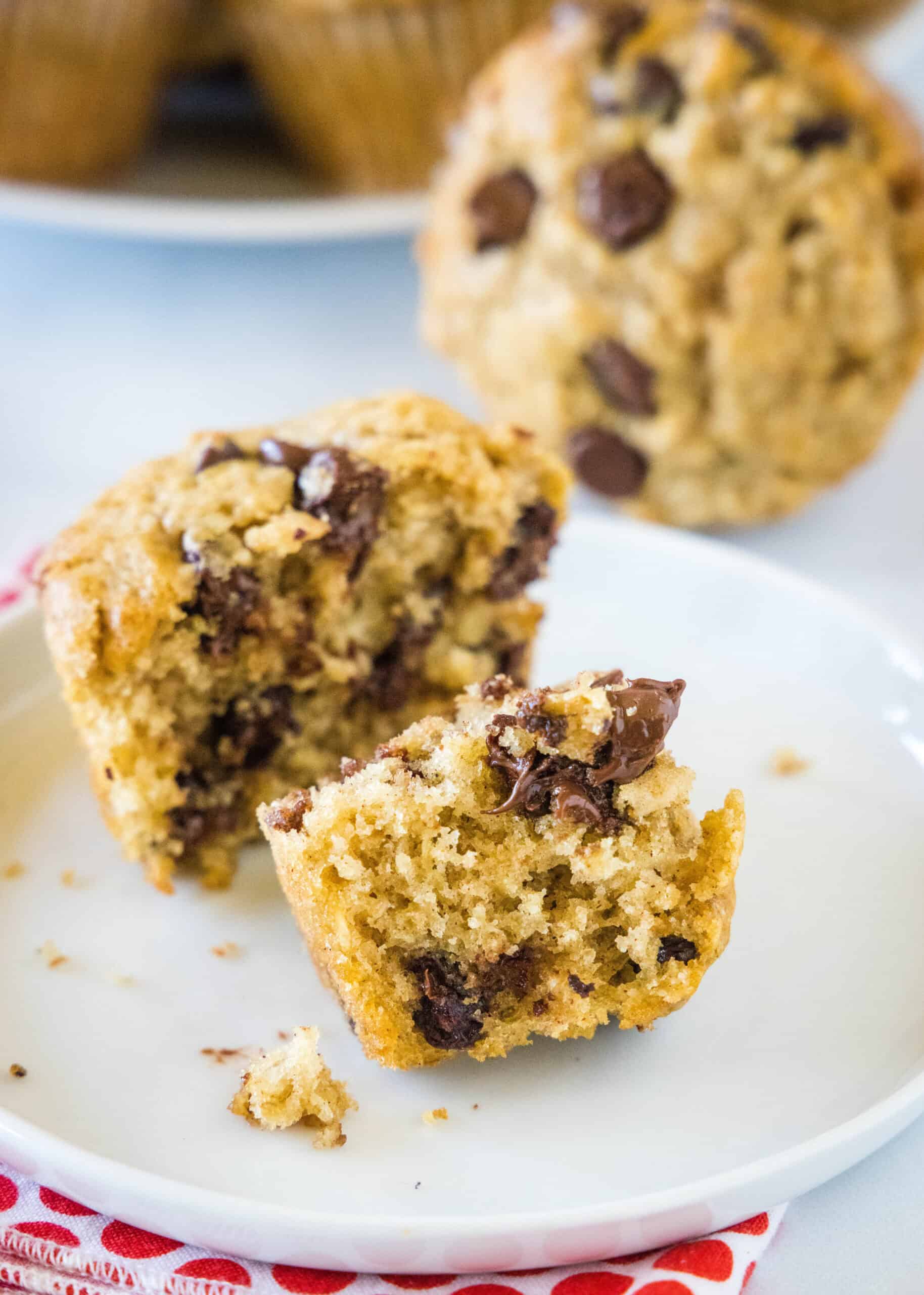 An oatmeal chocolate chip muffin broken in half on a white plate with more muffins in the background.