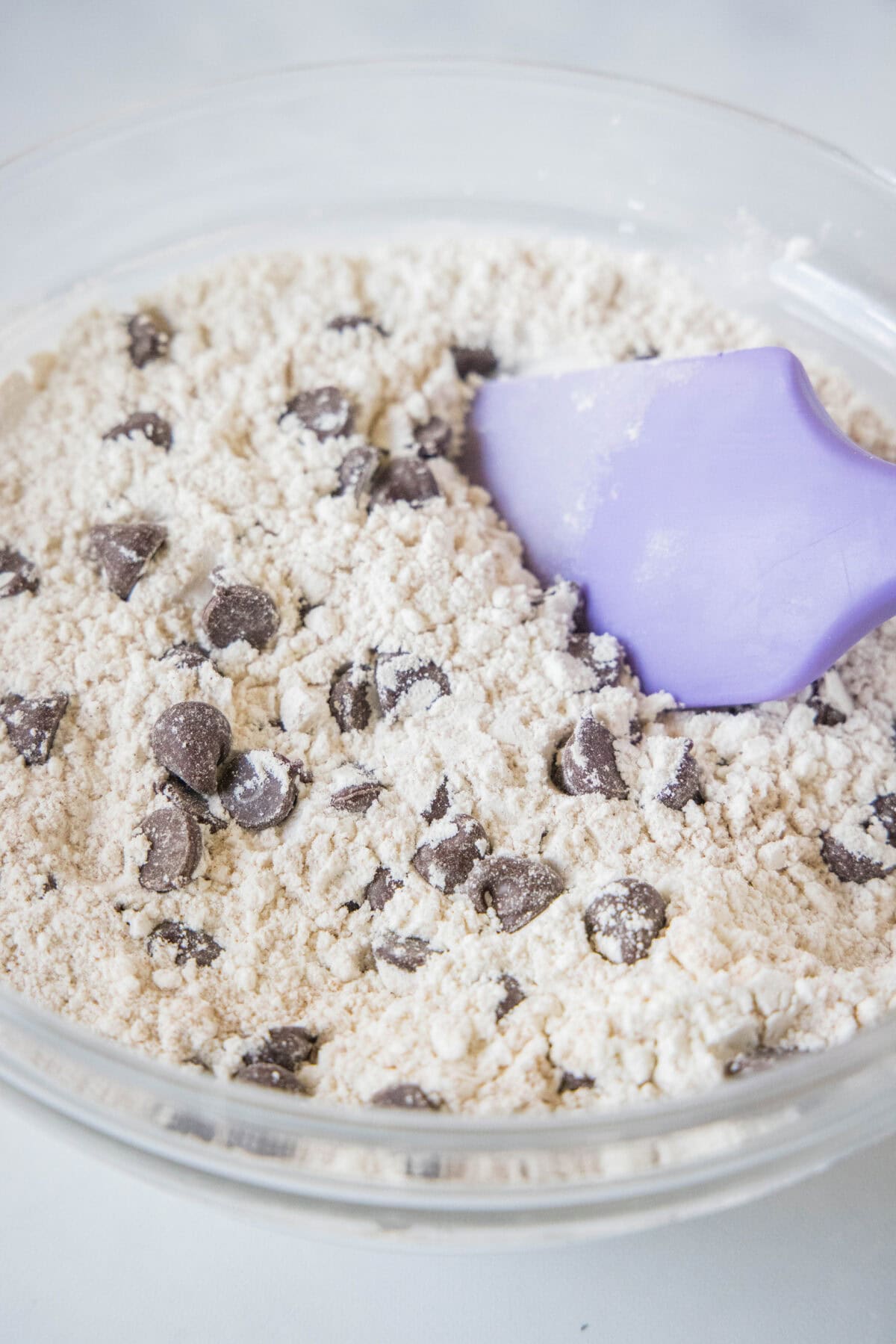 Chocolate chips folded into dry muffin ingredients in a glass bowl with a rubber spatula.