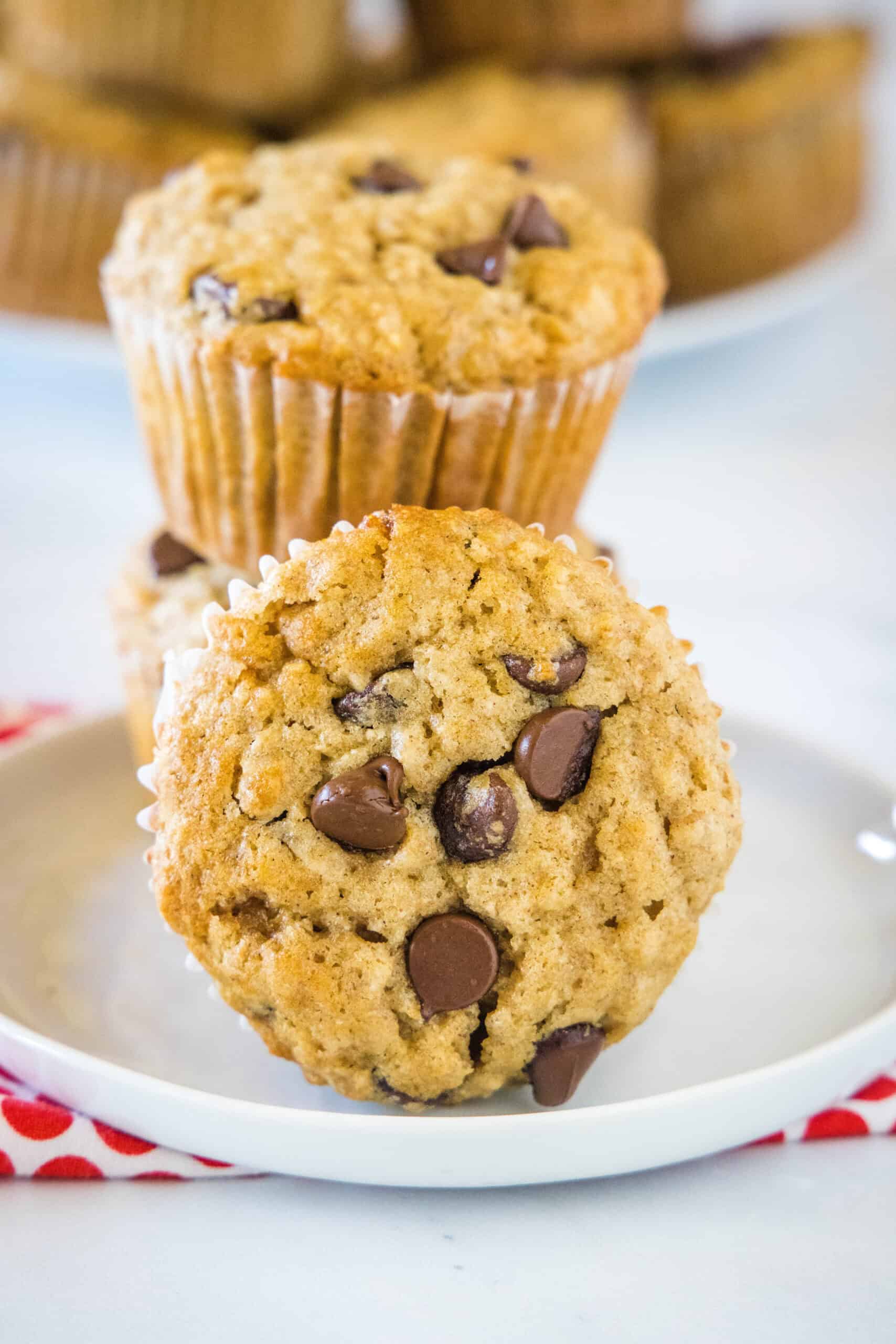 Two oatmeal chocolate chip muffins stacked on a white plate, with a third muffin on its side in the foreground.