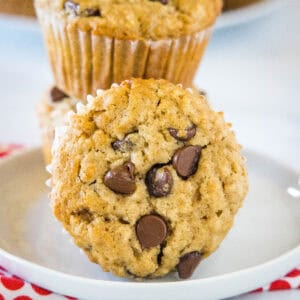 Two oatmeal chocolate chip muffins stacked on a white plate, with a third muffin on its side in the foreground.