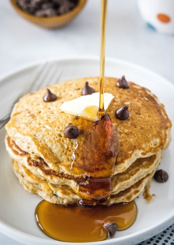 pouring syrup on a stack of pancakes
