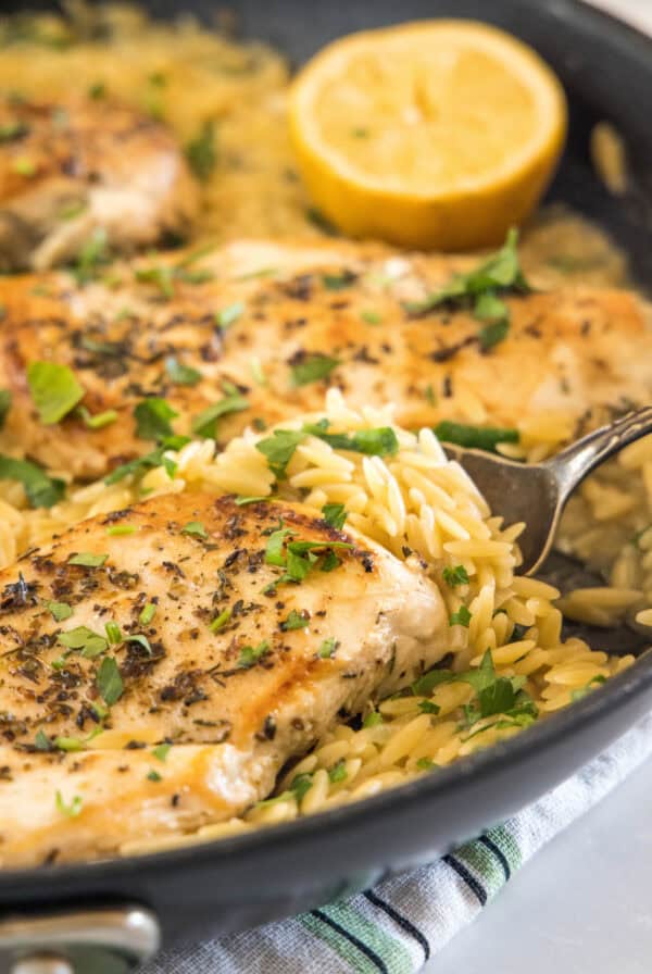 Close up of one pan chicken with orzo in a skillet with a serving spoon.