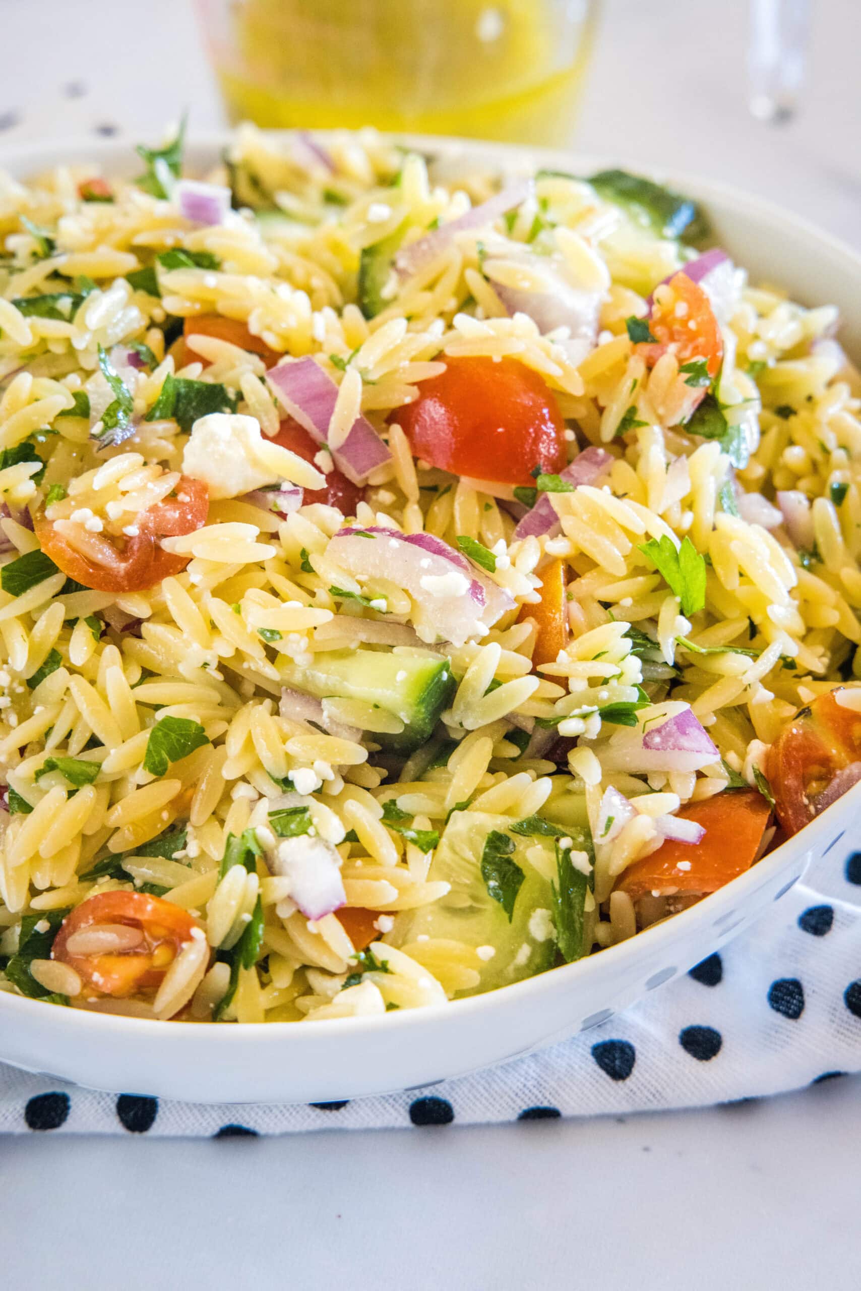 Orzo pasta salad in a large bowl resting on top of a black and white polka dot dishcloth.