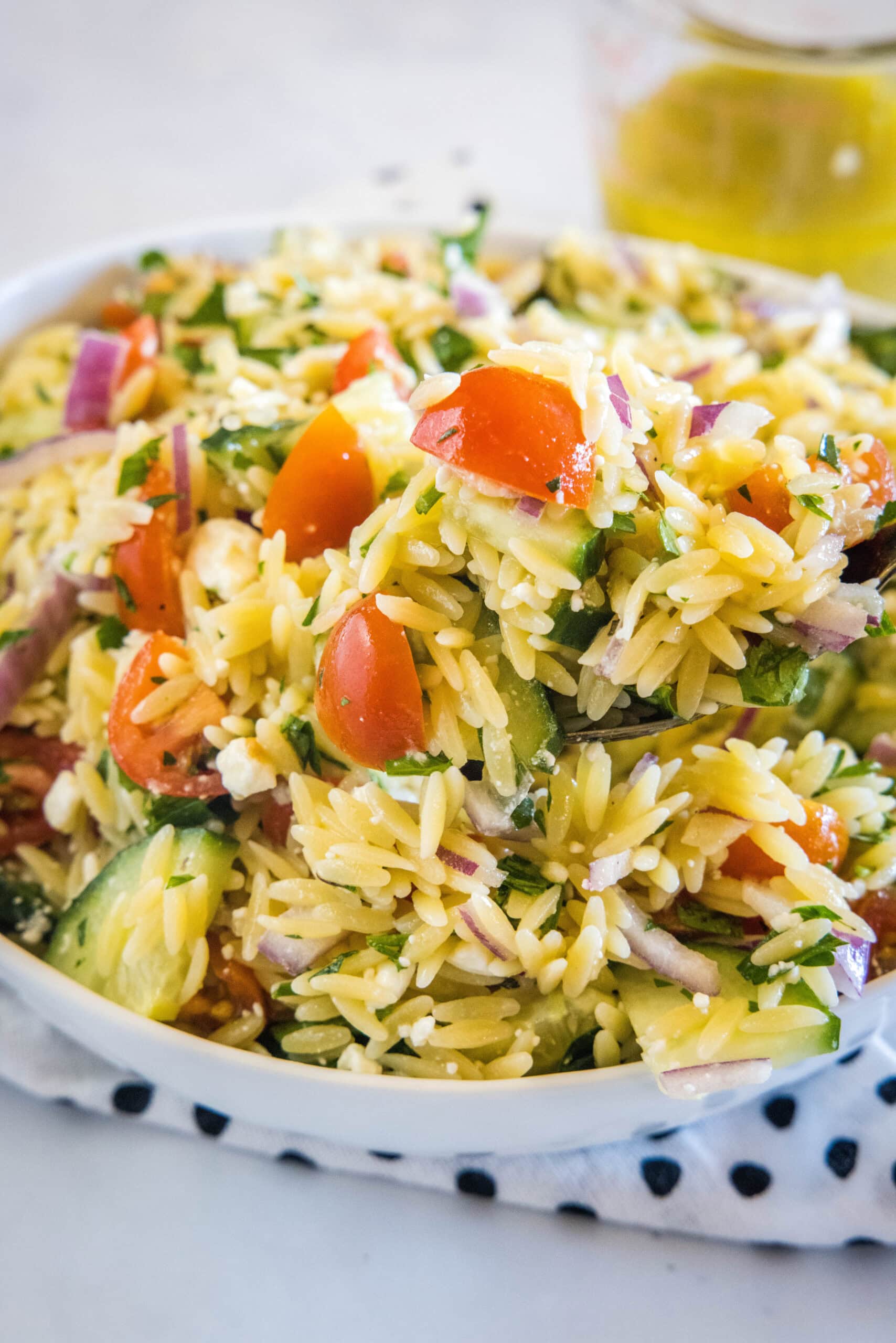 Orzo pasta salad in a large bowl resting on top of a black and white polka dot dishcloth.