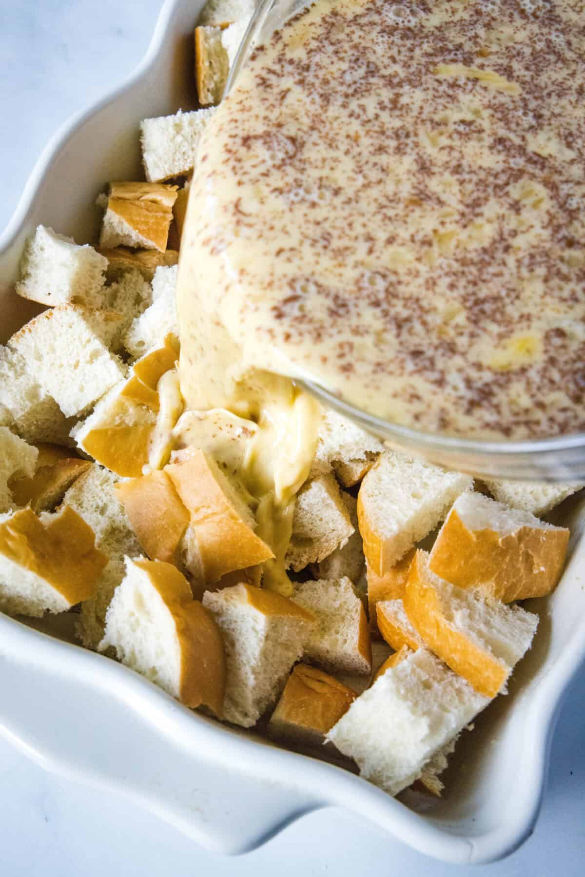 pouring egg custard over bread cubes