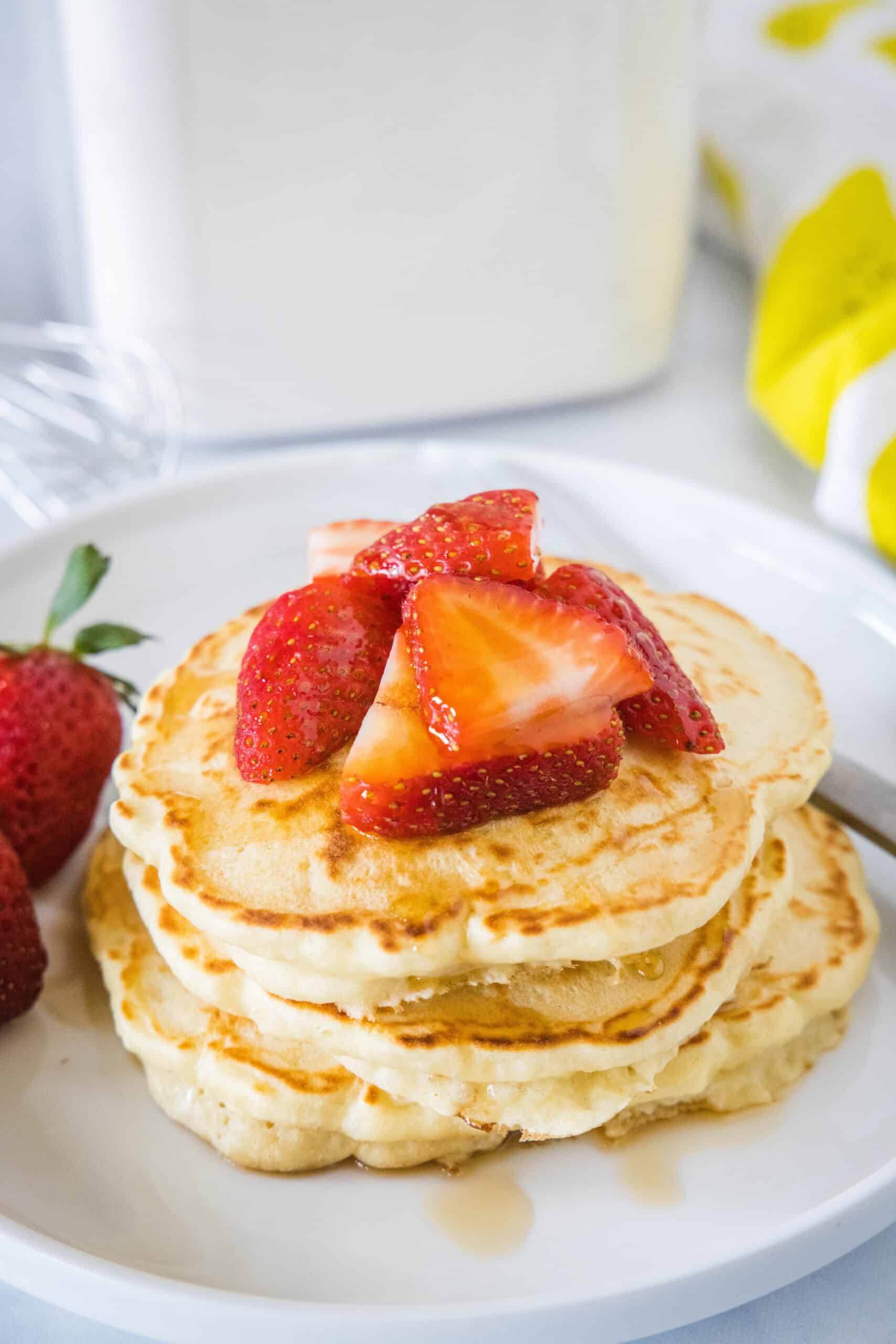 A stack of homemade pancakes topped with fresh strawberries and syrup on a white plate.