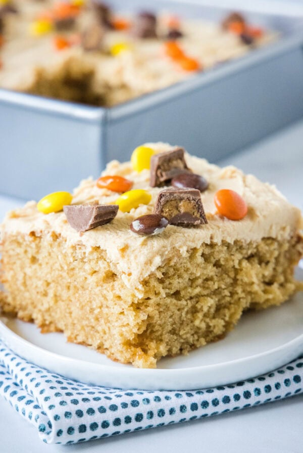 A slice of peanut butter cake topped with peanut butter frosting and chopped Reese's peanut butter cups on a plate.