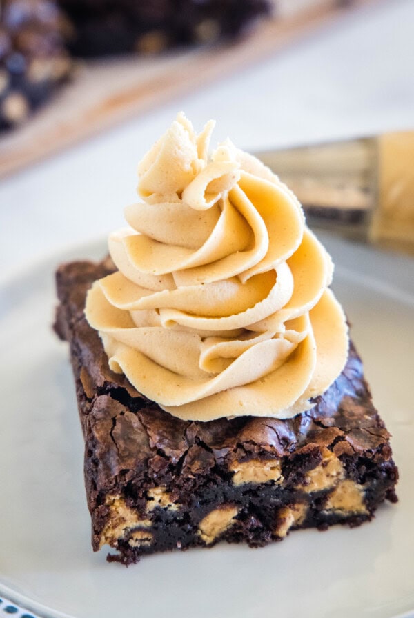 A chocolate brownie topped with a swirl of peanut butter frosting on a plate.