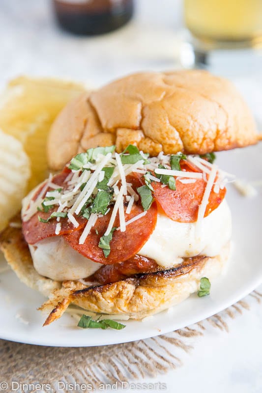 A close up of pepperoni pizza burger on a plate with potato chips