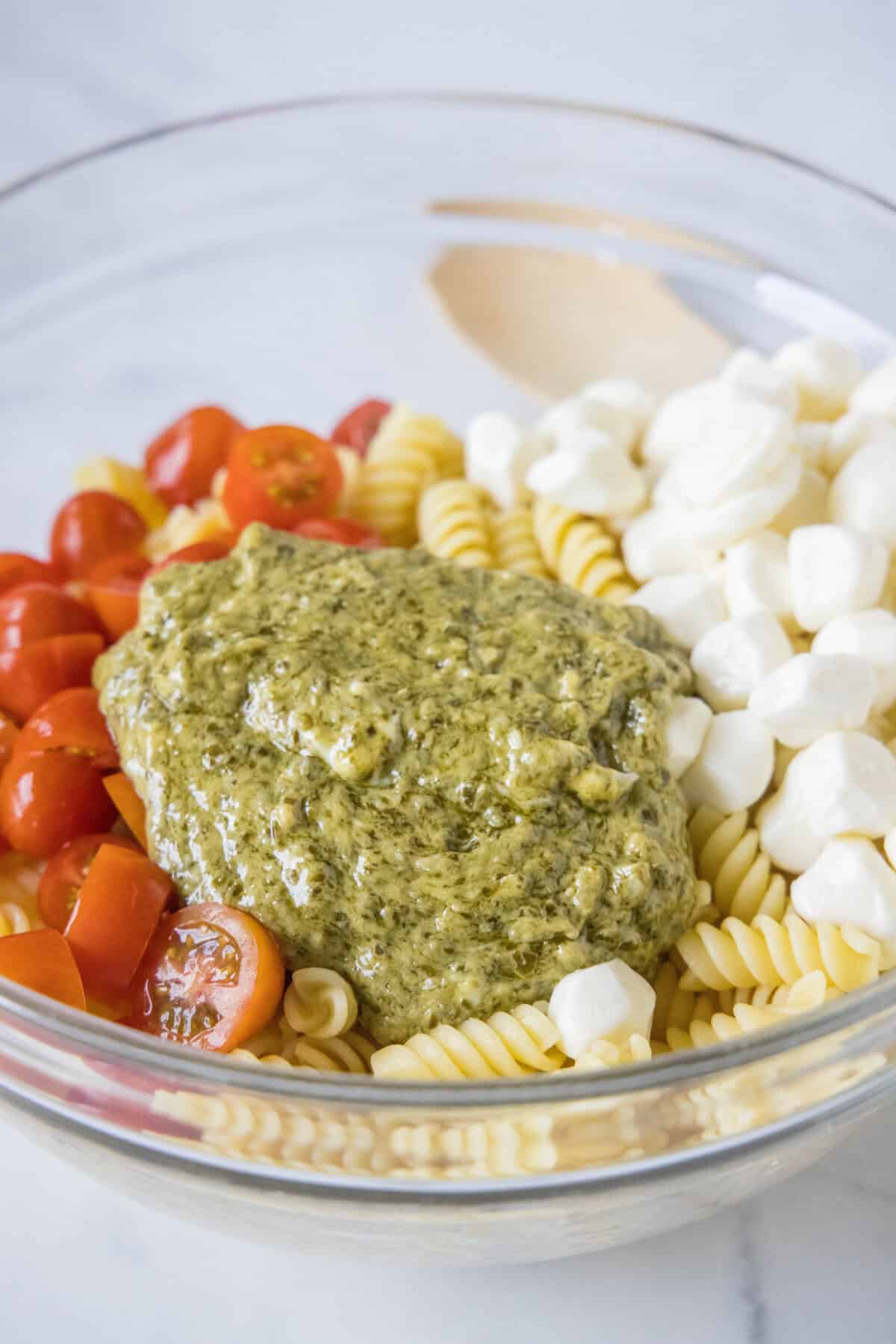 adding pesto dressing to pasta, tomatoes and mozzarella
