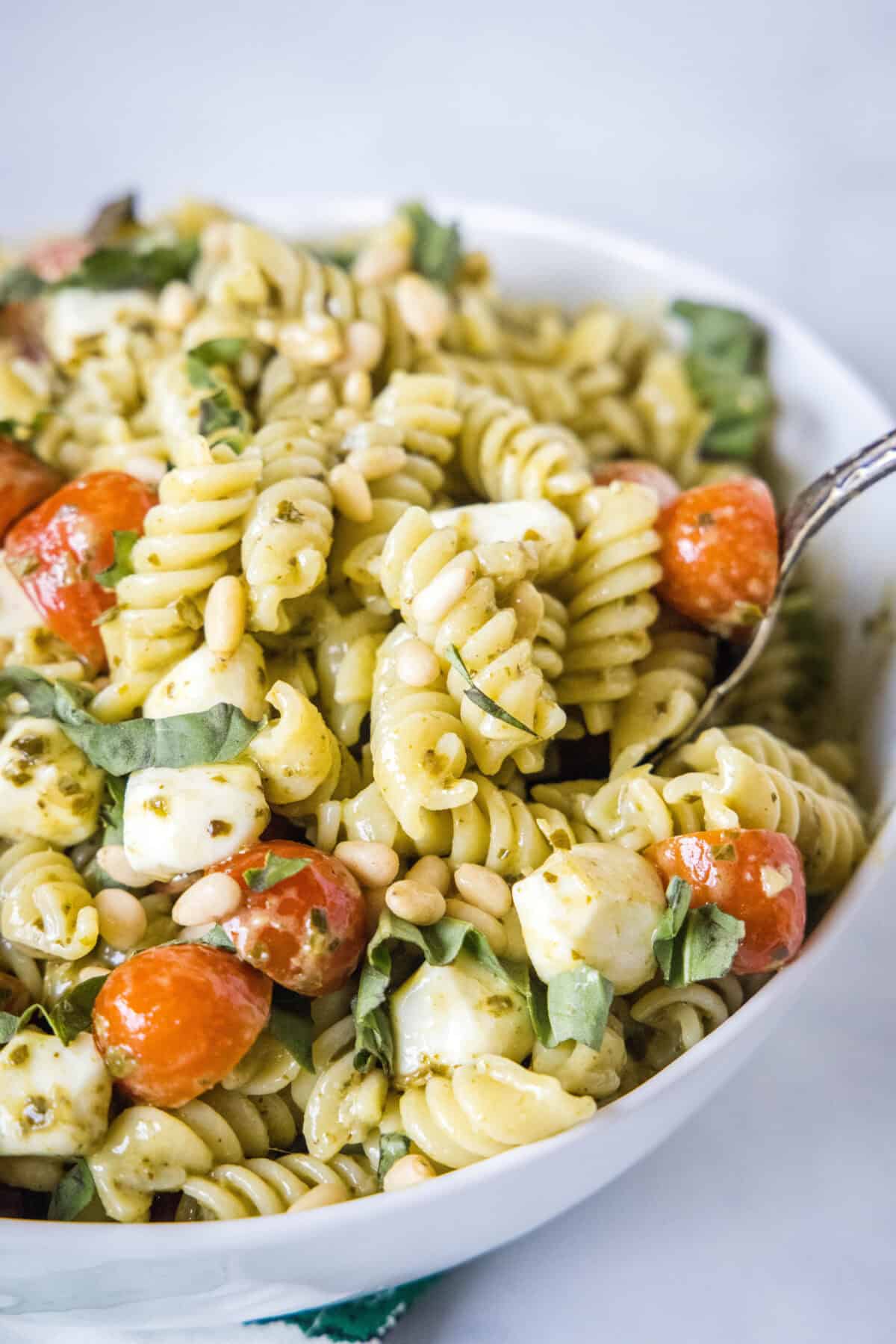 a spoon scooping out pesto pasta salad from a serving bowl