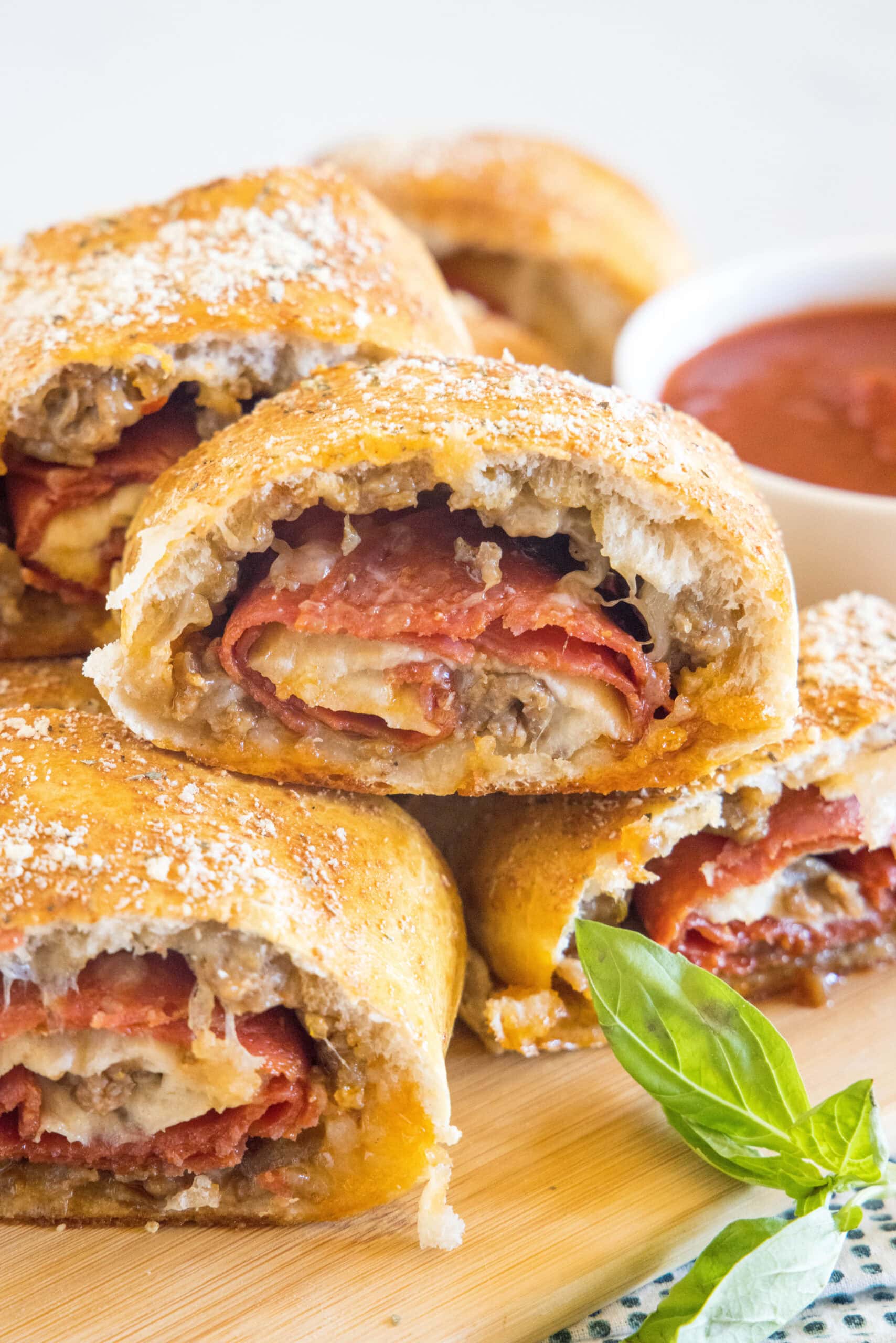 Pizza bread slices stacked on a wooden board next to a bowl of pizza sauce for dipping.