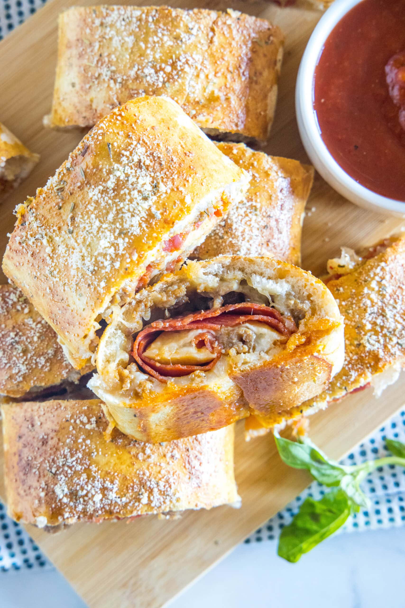 Overhead view of pizza bread slices stacked on a wooden board next to a bowl of pizza sauce for dipping.