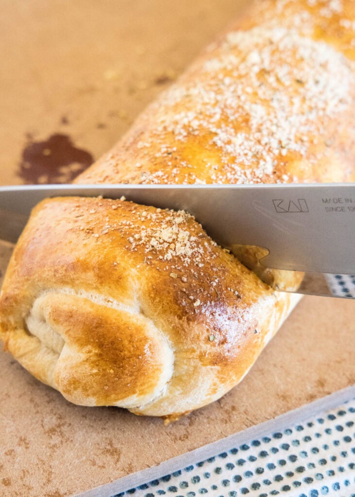 A knife slicing into the end of a baked pizza bread roll.