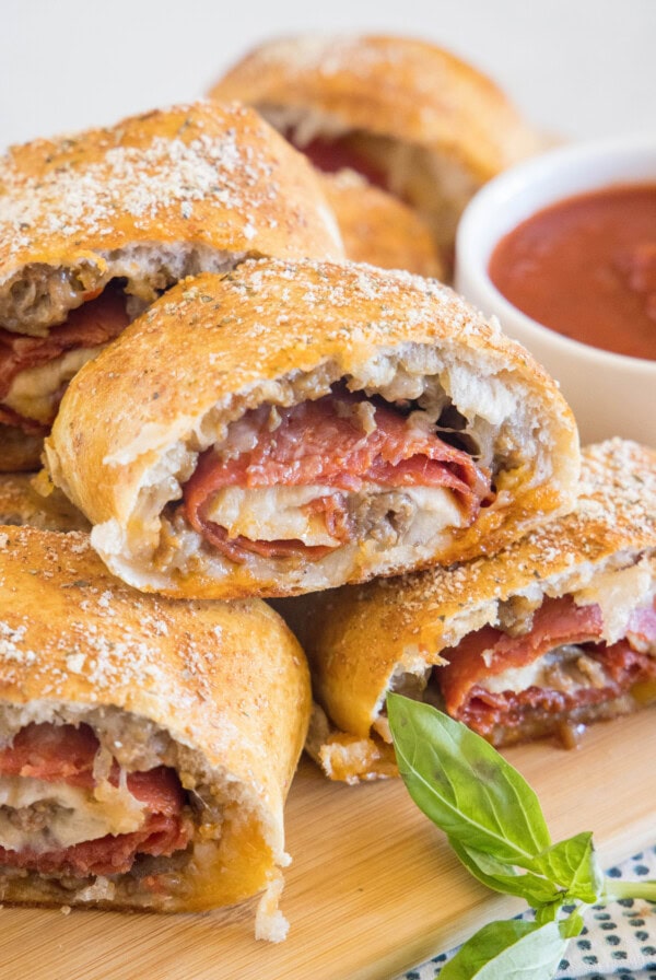Pizza bread slices stacked on a wooden board next to a bowl of pizza sauce for dipping.