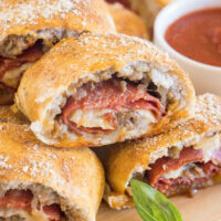 Pizza bread slices stacked on a wooden board next to a bowl of pizza sauce for dipping.
