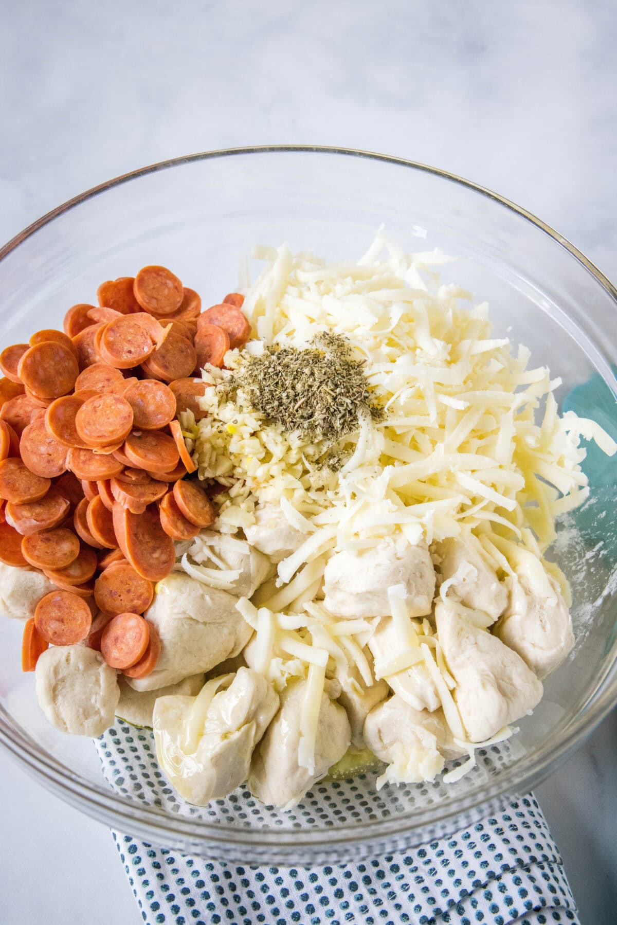 Pizza monkey bread ingredients combined in a glass bowl.