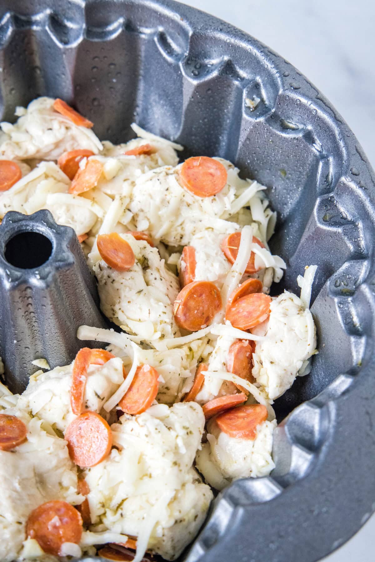 Biscuit dough balls and pizza ingredients combined in a bundt pan.