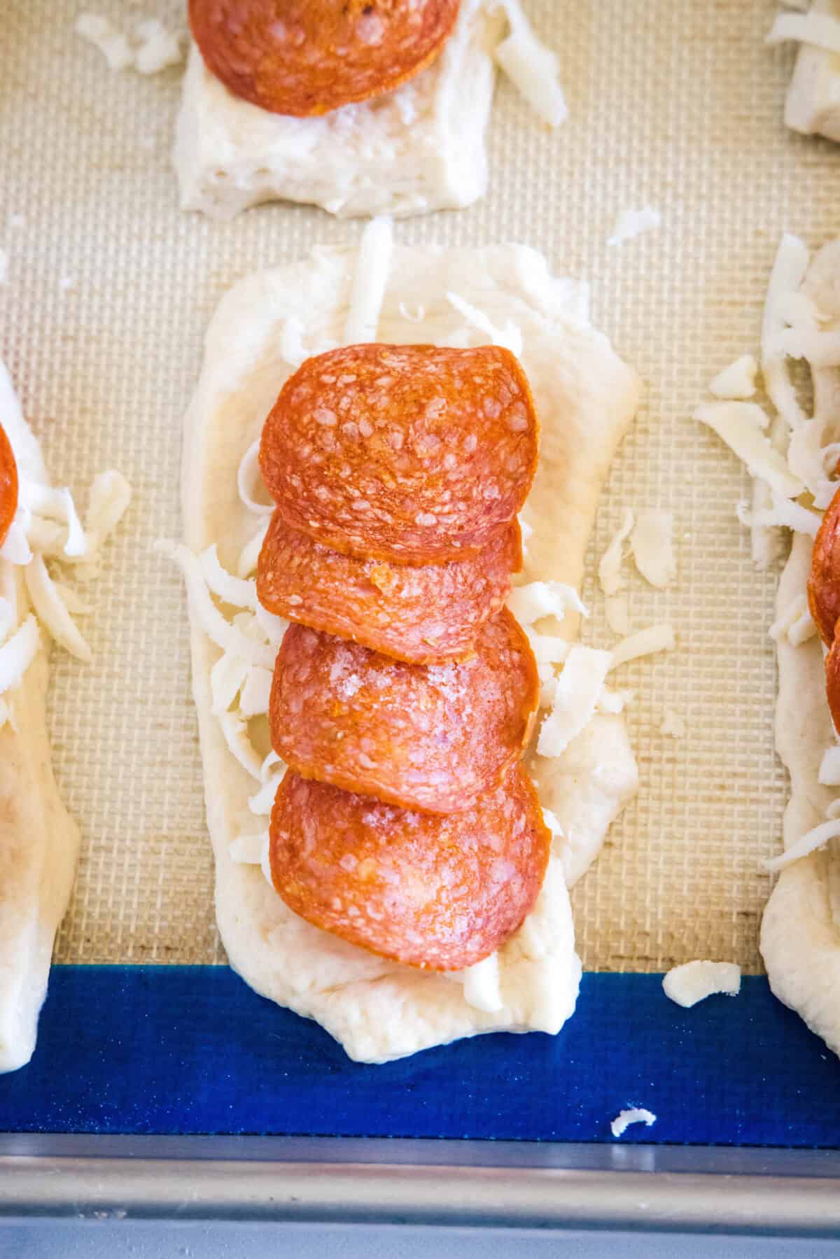 Overhead view of shredded mozzarella and pepperoni slices layered over a rolled out piece of pizza dough on a baking sheet.