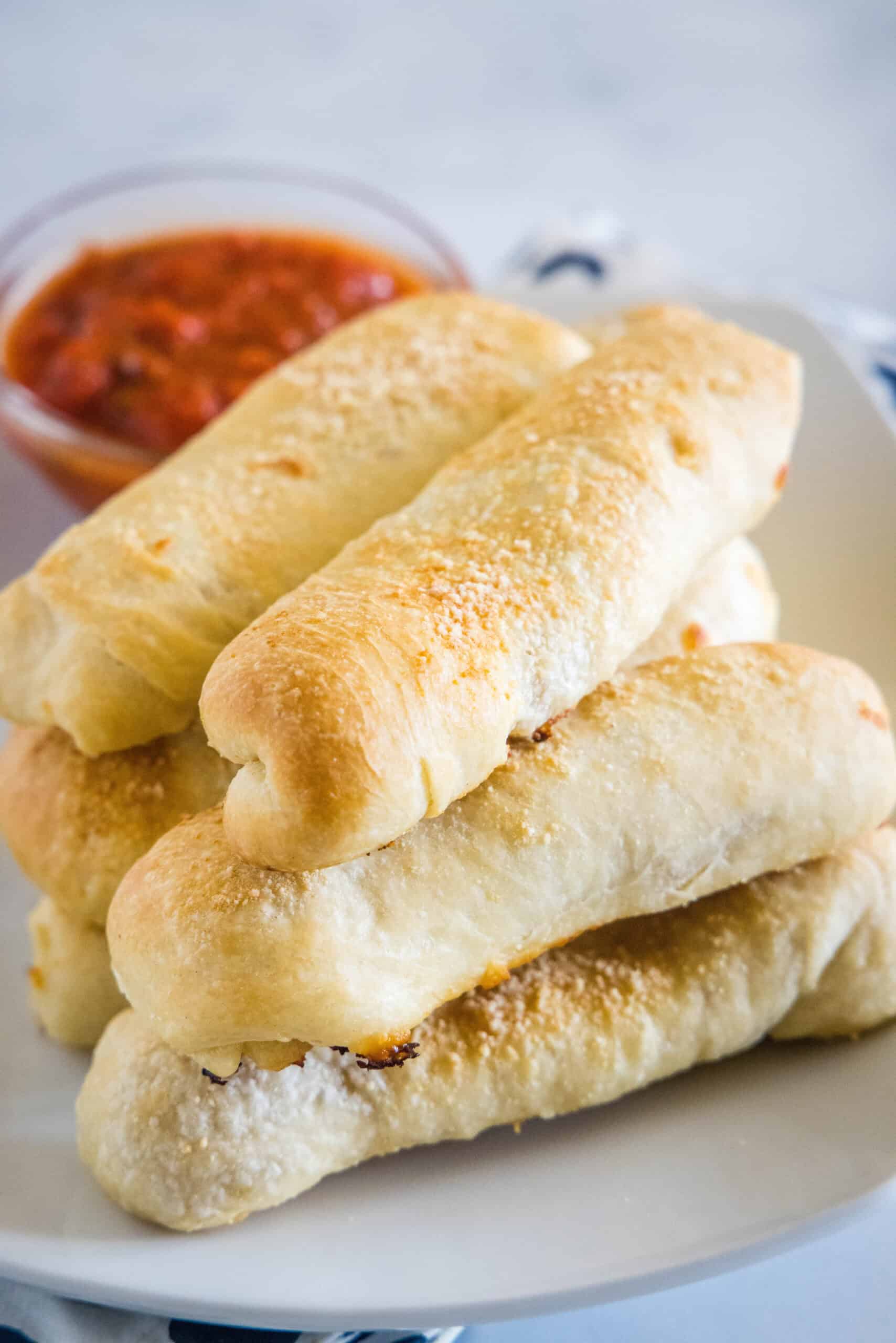 Pepperoni rolls stacked on a plate with a small bowl of marinara sauce in the background.